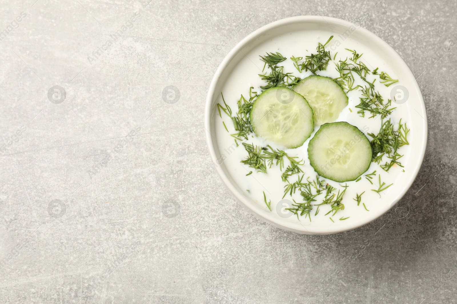 Tasty cucumber soup with dill in bowl on grey textured table, top view. Space for text Photo of Tasty cucumber soup with dill in bowl on grey textured table, top view. Space for text