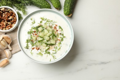 Photo of Tasty cucumber soup with dill and nuts in bowl among products on white marble table, flat lay. Space for text