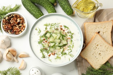Photo of Tasty cucumber soup with dill and nuts in bowl among products on white table, flat lay