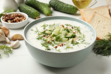 Photo of Tasty cucumber soup with dill and nuts in bowl on white table, closeup