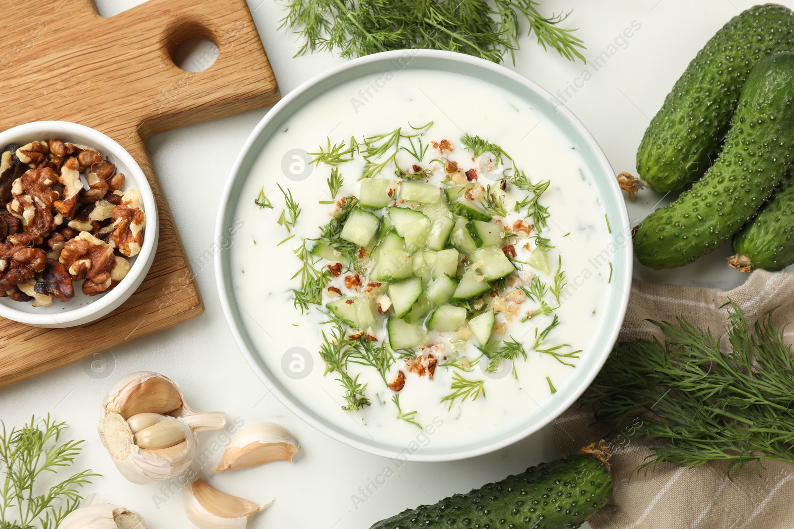 Tasty cucumber soup with dill and nuts in bowl among products on white table, flat lay Photo of Tasty cucumber soup with dill and nuts in bowl among products on white table, flat lay