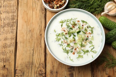Photo of Tasty cucumber soup with dill, nuts and garlic on wooden table, flat lay. Space for text