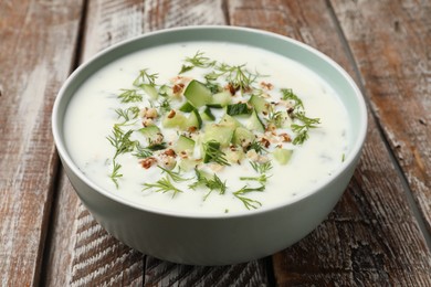 Photo of Tasty cucumber soup with dill and nuts in bowl on wooden table, closeup