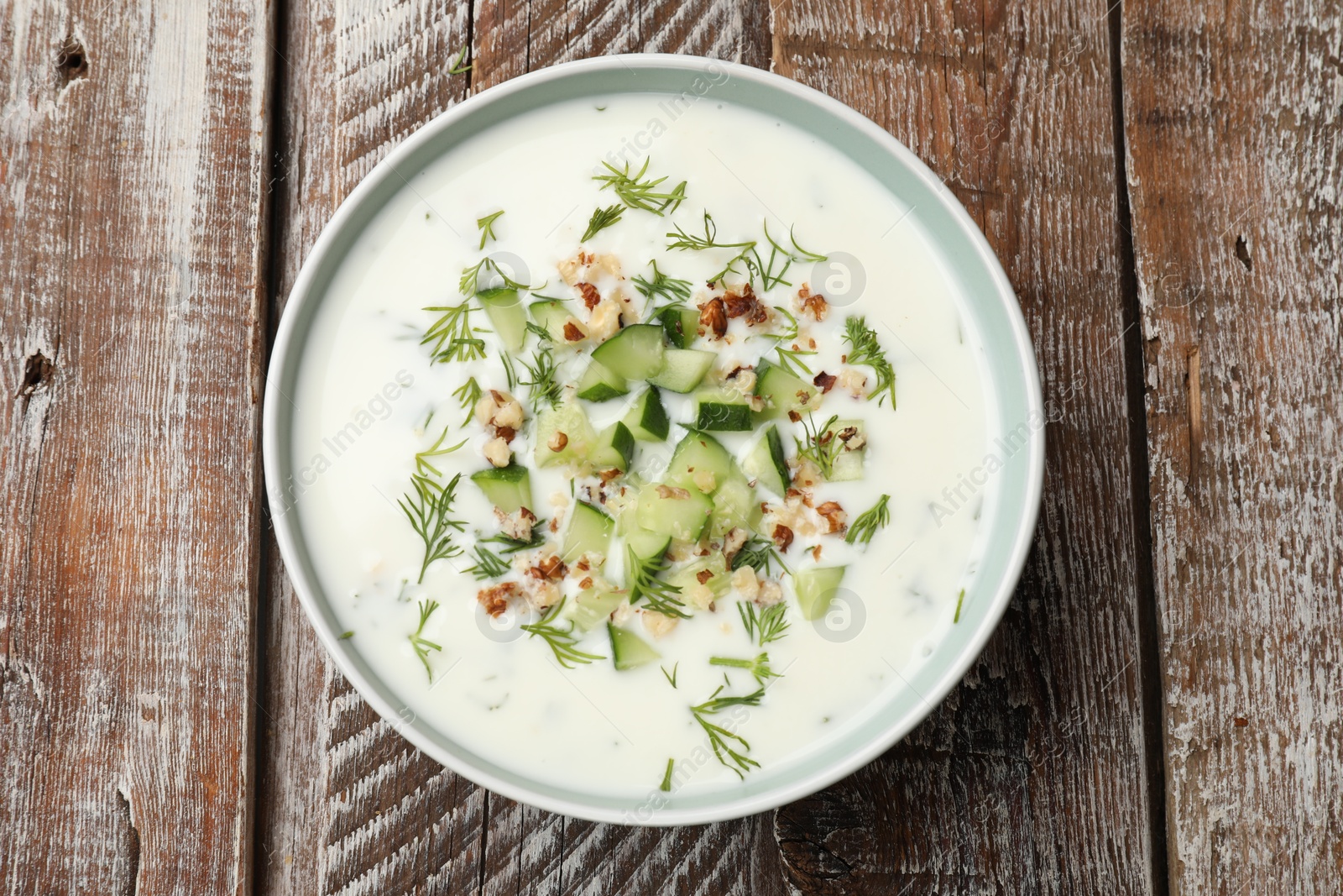 Tasty cucumber soup with dill and nuts in bowl on wooden table, top view Photo of Tasty cucumber soup with dill and nuts in bowl on wooden table, top view