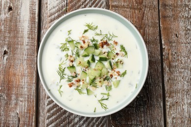 Photo of Tasty cucumber soup with dill and nuts in bowl on wooden table, top view