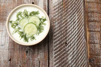 Photo of Tasty cucumber soup with dill in bowl on wooden table, top view. Space for text