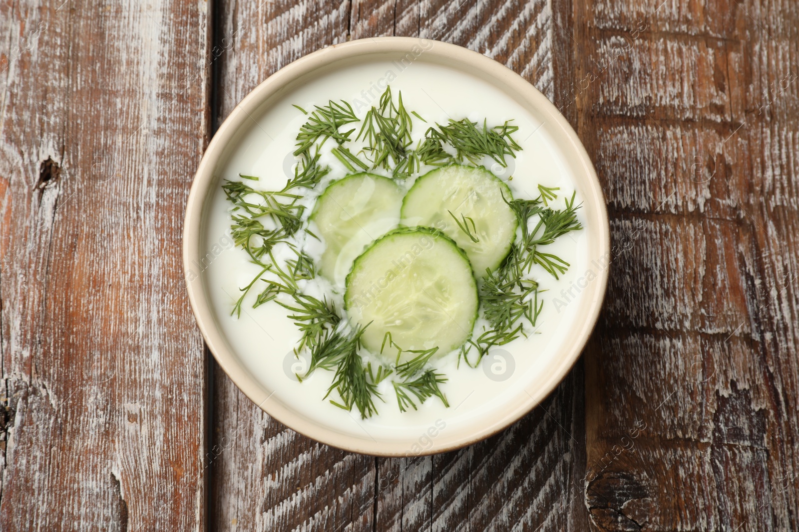 Tasty cucumber soup with dill in bowl on wooden table, top view Photo of Tasty cucumber soup with dill in bowl on wooden table, top view