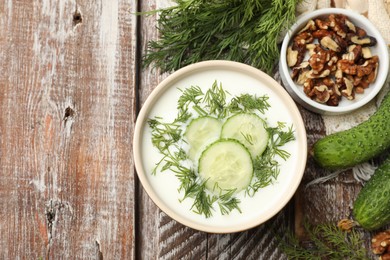 Photo of Tasty cucumber soup with dill and nuts on wooden table, flat lay. Space for text