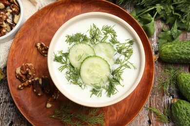 Photo of Tasty cucumber soup with dill and nuts on wooden table, flat lay