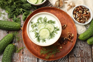 Photo of Tasty cucumber soup with dill and nuts on wooden table, flat lay