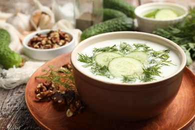 Photo of Tasty cucumber soup with dill and nuts on wooden table, closeup
