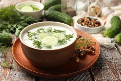 Photo of Tasty cucumber soup with dill and nuts on wooden table, closeup