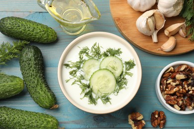 Photo of Tasty cucumber soup with dill among products on light blue wooden table, flat lay