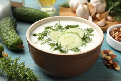 Photo of Tasty cucumber soup with dill among products on light blue wooden table, closeup
