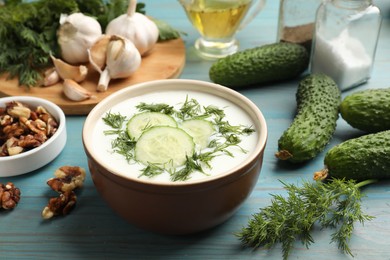 Photo of Tasty cucumber soup with dill among products on light blue wooden table, closeup