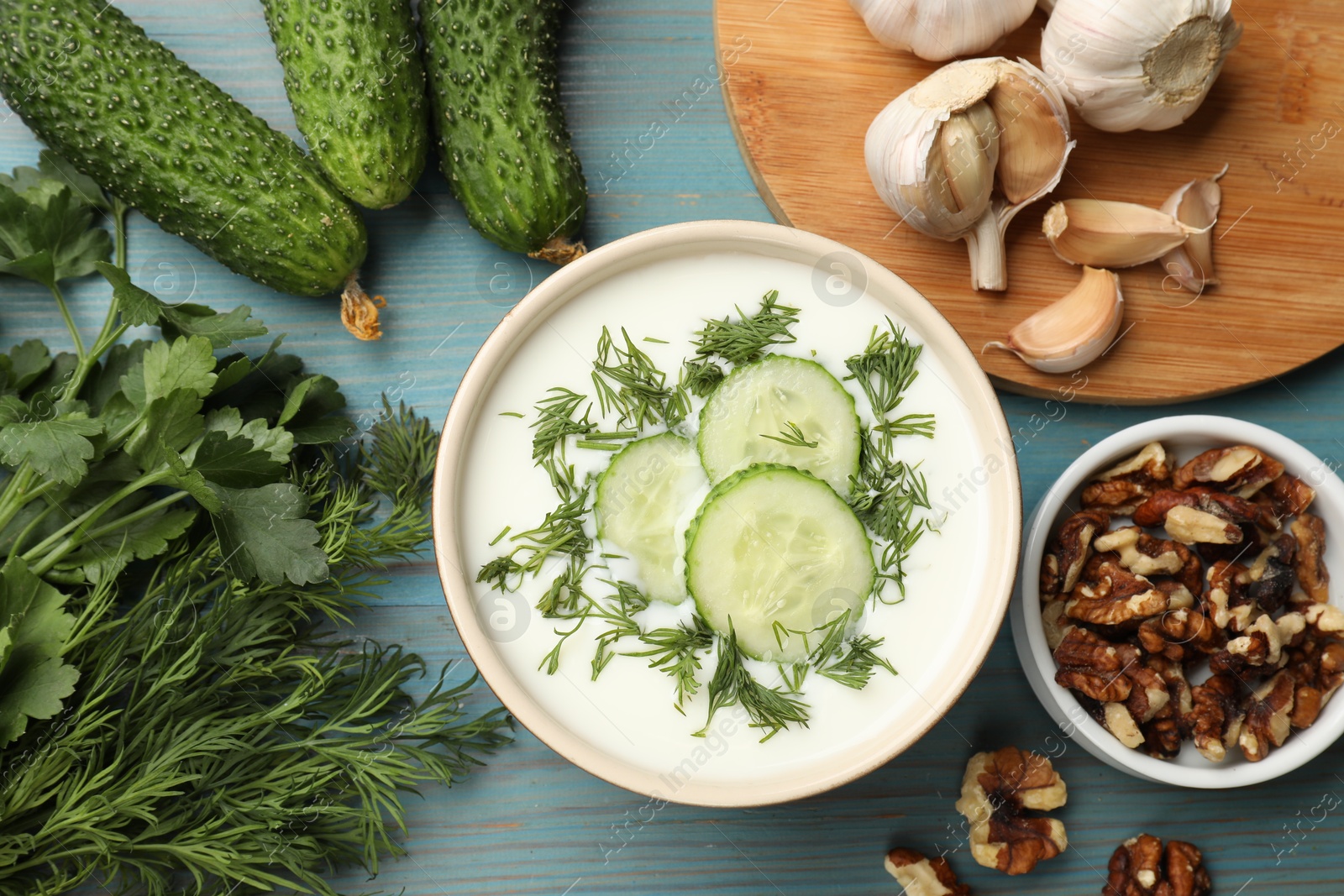 Tasty cucumber soup with dill among products on light blue wooden table, flat lay Photo of Tasty cucumber soup with dill among products on light blue wooden table, flat lay