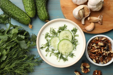 Photo of Tasty cucumber soup with dill among products on light blue wooden table, flat lay