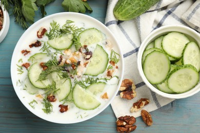 Photo of Tasty cucumber soup with dill and nuts in bowl on light blue wooden table, flat lay