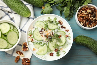 Photo of Tasty cucumber soup with dill and nuts in bowl on light blue wooden table, flat lay