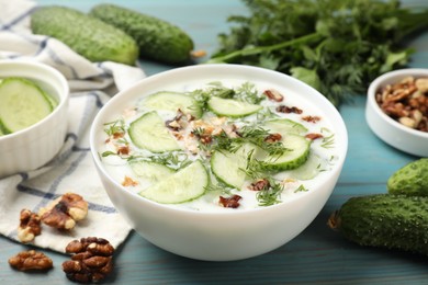Photo of Tasty cucumber soup with dill and nuts in bowl on light blue wooden table, closeup