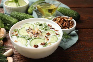 Photo of Tasty cucumber soup with dill and nuts in bowl on wooden table, closeup