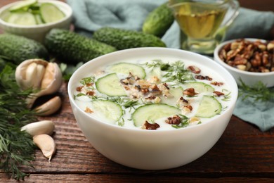 Photo of Tasty cucumber soup with dill and nuts in bowl on wooden table, closeup