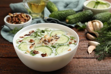 Photo of Tasty cucumber soup with dill and nuts in bowl on wooden table, closeup