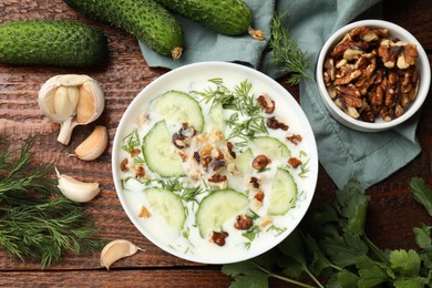 Photo of Tasty cucumber soup with dill, nuts and garlic on wooden table, flat lay