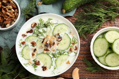 Photo of Tasty cucumber soup with dill, nuts and garlic on wooden table, flat lay