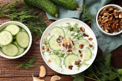 Photo of Tasty cucumber soup with dill, nuts and garlic on wooden table, flat lay