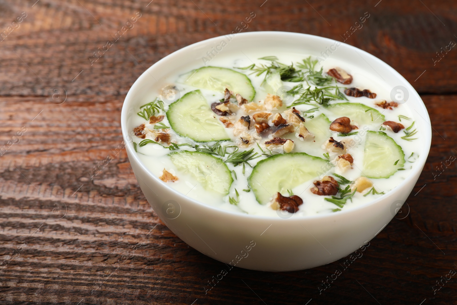 Tasty cucumber soup with dill and nuts in bowl on wooden table, closeup Photo of Tasty cucumber soup with dill and nuts in bowl on wooden table, closeup