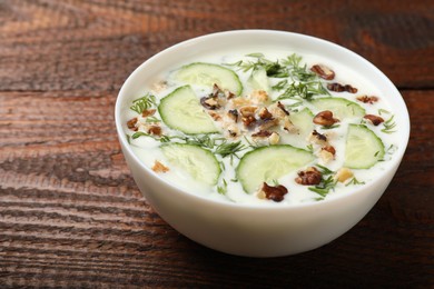 Photo of Tasty cucumber soup with dill and nuts in bowl on wooden table, closeup