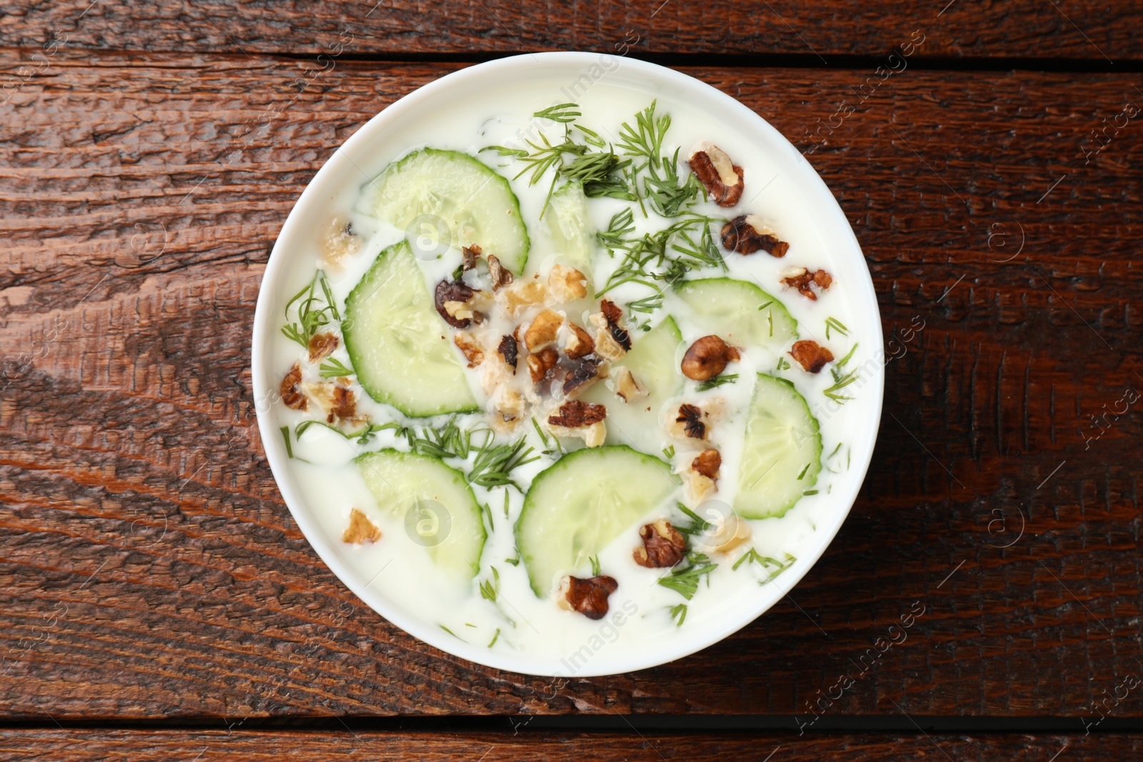 Tasty cucumber soup with dill and nuts in bowl on wooden table, top view Photo of Tasty cucumber soup with dill and nuts in bowl on wooden table, top view