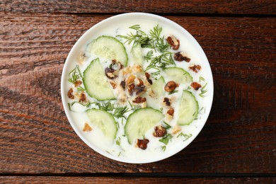 Photo of Tasty cucumber soup with dill and nuts in bowl on wooden table, top view