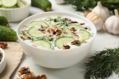 Photo of Tasty cucumber soup with dill and nuts in bowl on white table, closeup