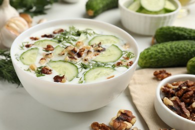 Photo of Tasty cucumber soup with dill and nuts in bowl on white table, closeup