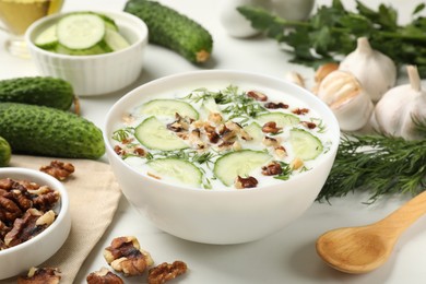 Photo of Tasty cucumber soup with dill and nuts in bowl on white table, closeup