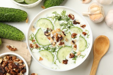 Photo of Tasty cucumber soup with dill, nuts and garlic on white table, flat lay