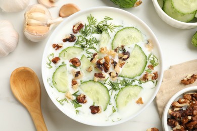 Photo of Tasty cucumber soup with dill, nuts and garlic on white table, flat lay