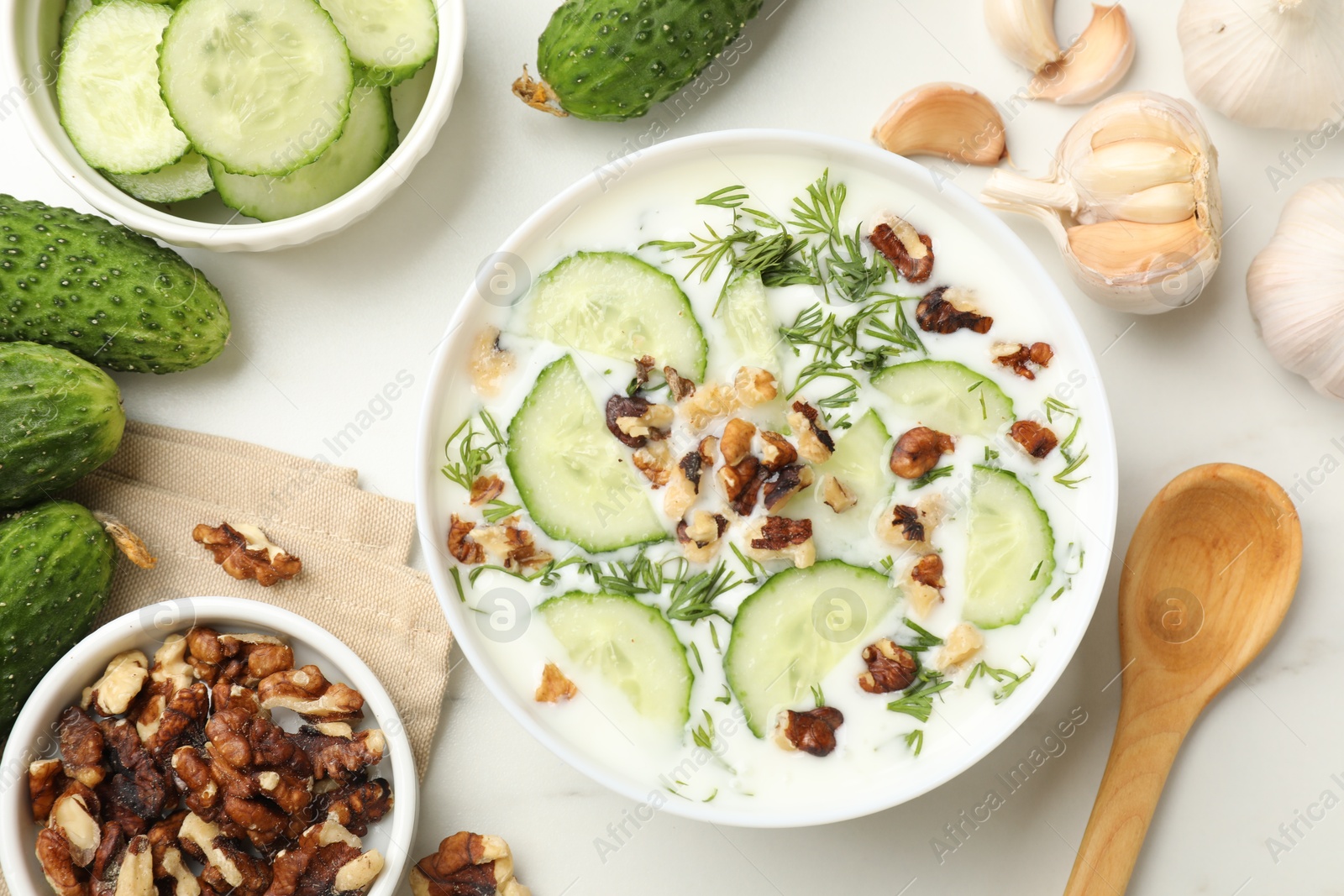 Tasty cucumber soup with dill, nuts and garlic on white table, flat lay Photo of Tasty cucumber soup with dill, nuts and garlic on white table, flat lay