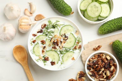 Photo of Tasty cucumber soup with dill, nuts and garlic on white table, flat lay
