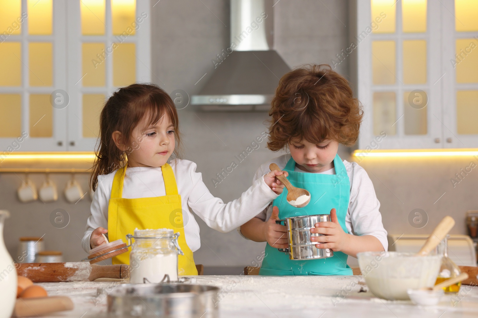 Cooking recipe. Cute children sieving flour at table in kitchen Photo of Cooking recipe. Cute children sieving flour at table in kitchen