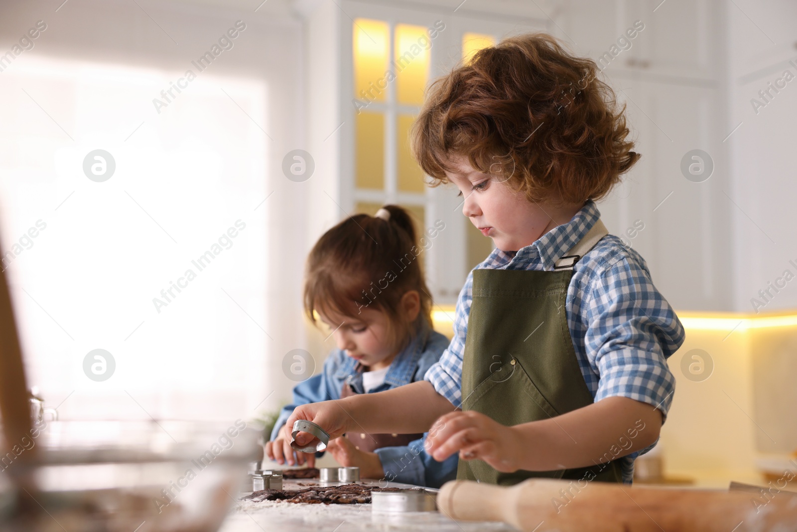 Cooking recipe. Little children cutting cookies with cutters at table in kitchen. Space for text Photo of Cooking recipe. Little children cutting cookies with cutters at table in kitchen. Space for text