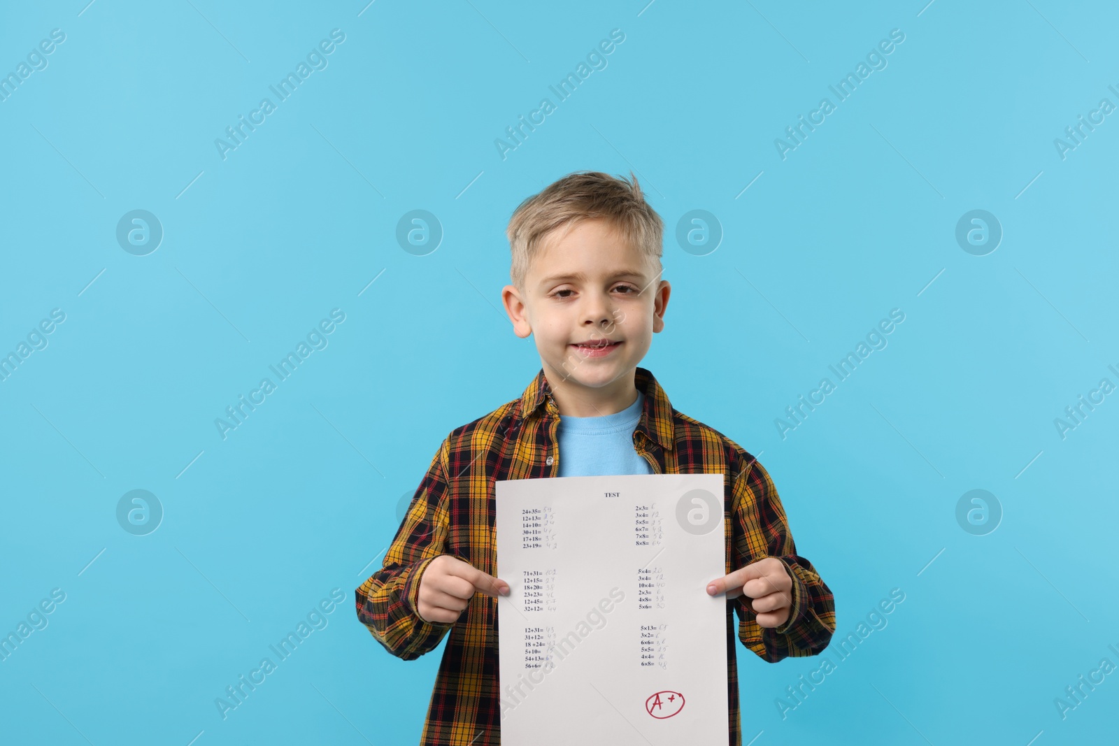 School grade. Little boy holding answer sheet with letter A and plus symbol on light blue background Photo of School grade. Little boy holding answer sheet with letter A and plus symbol on light blue background