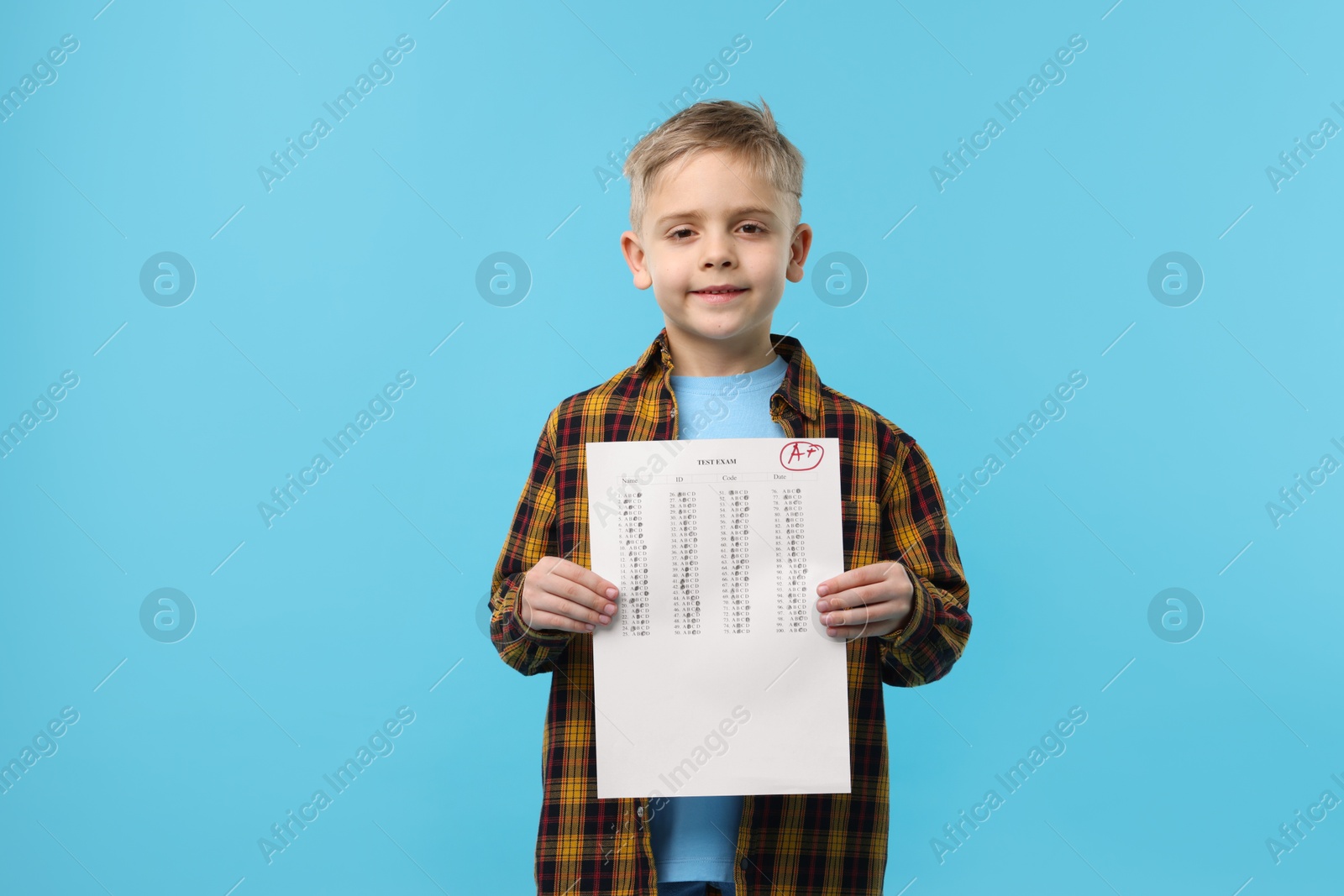 School grade. Little boy holding answer sheet with letter A and plus symbol on light blue background Photo of School grade. Little boy holding answer sheet with letter A and plus symbol on light blue background