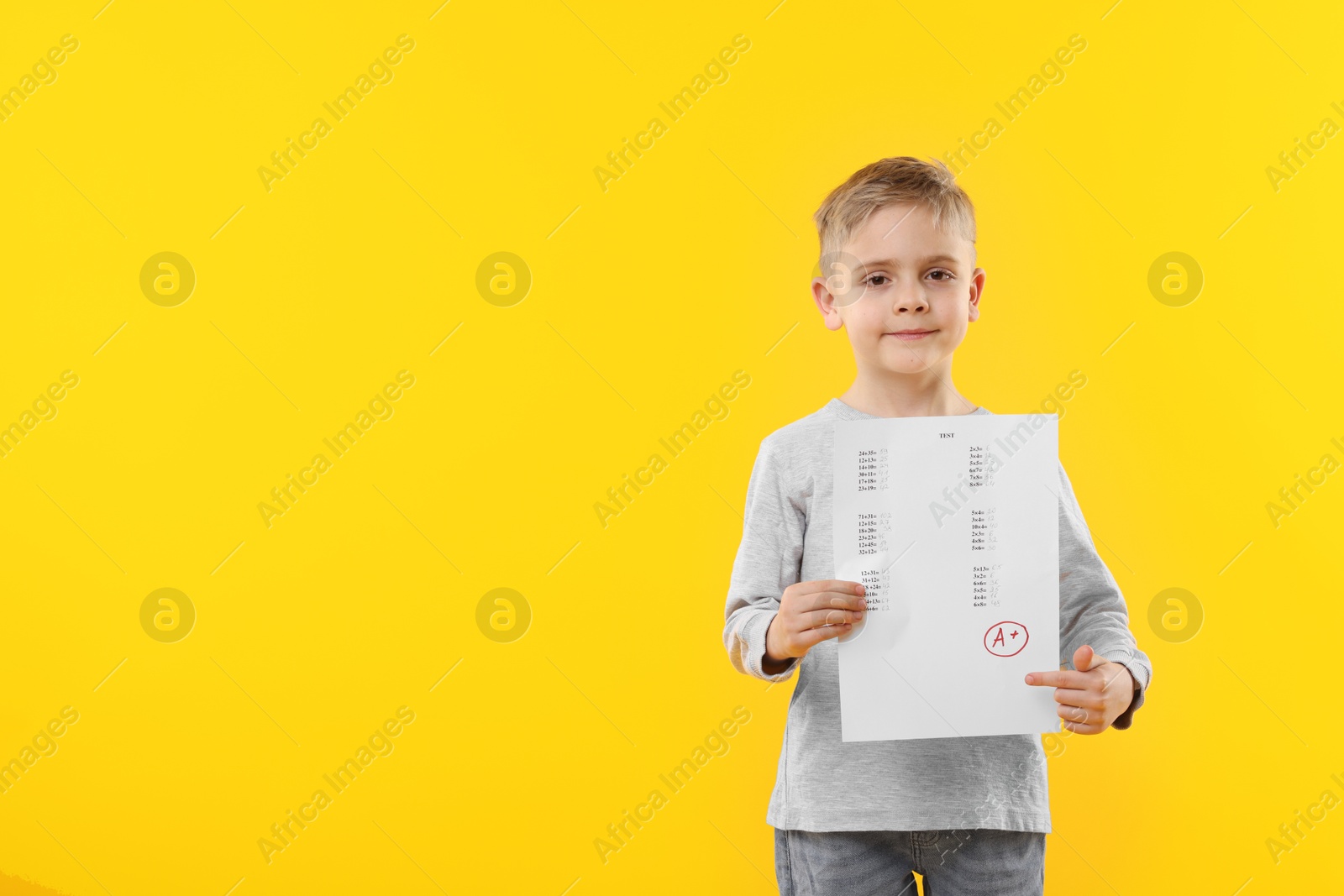 School grade. Little boy holding answer sheet with letter A and plus symbol on yellow background, space for text Photo of School grade. Little boy holding answer sheet with letter A and plus symbol on yellow background, space for text