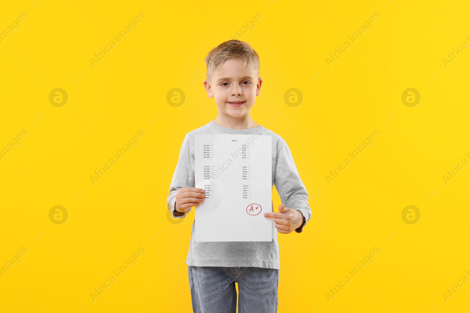 School grade. Little boy holding answer sheet with letter A and plus symbol on yellow background Photo of School grade. Little boy holding answer sheet with letter A and plus symbol on yellow background