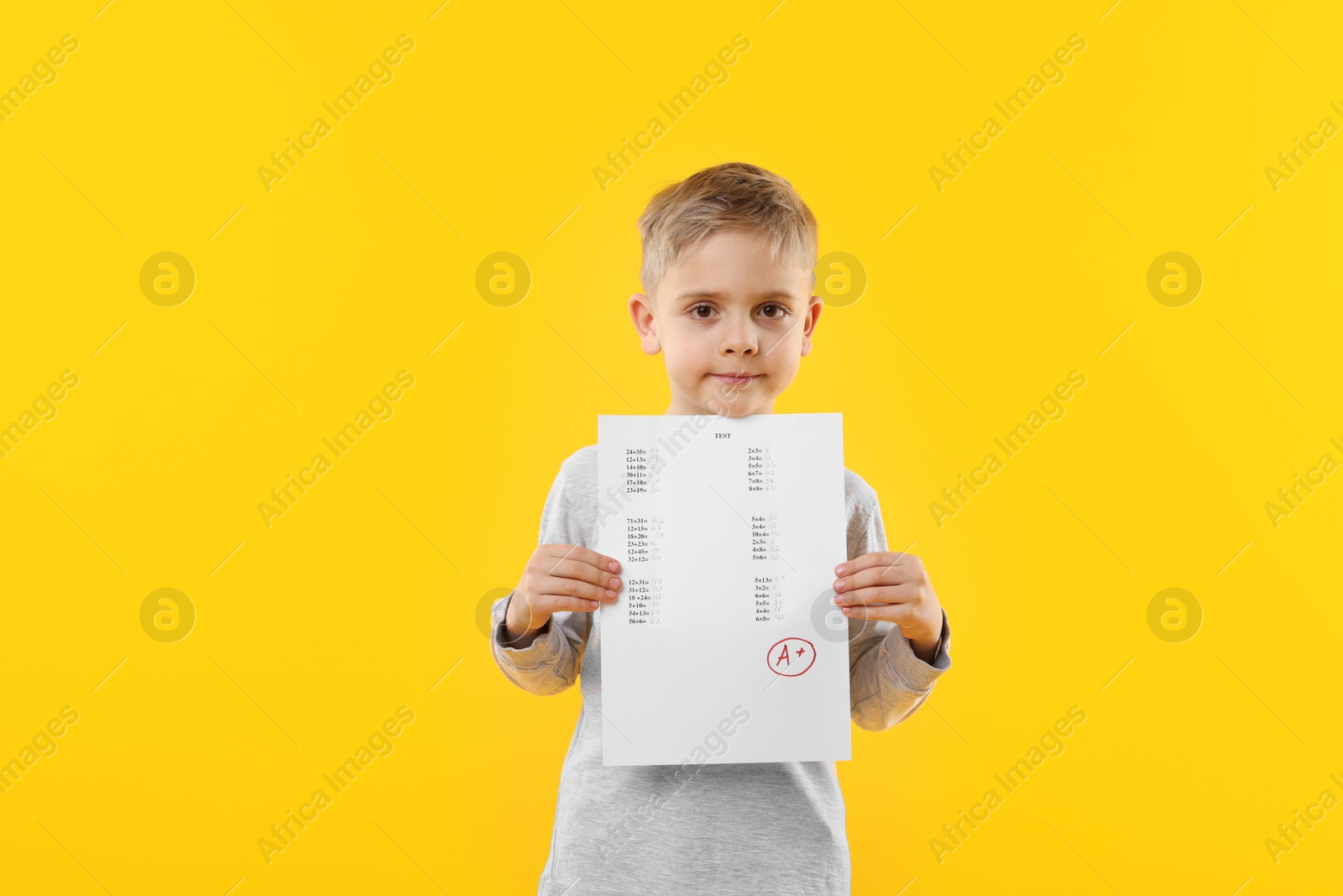 School grade. Little boy holding answer sheet with letter A and plus symbol on yellow background Photo of School grade. Little boy holding answer sheet with letter A and plus symbol on yellow background