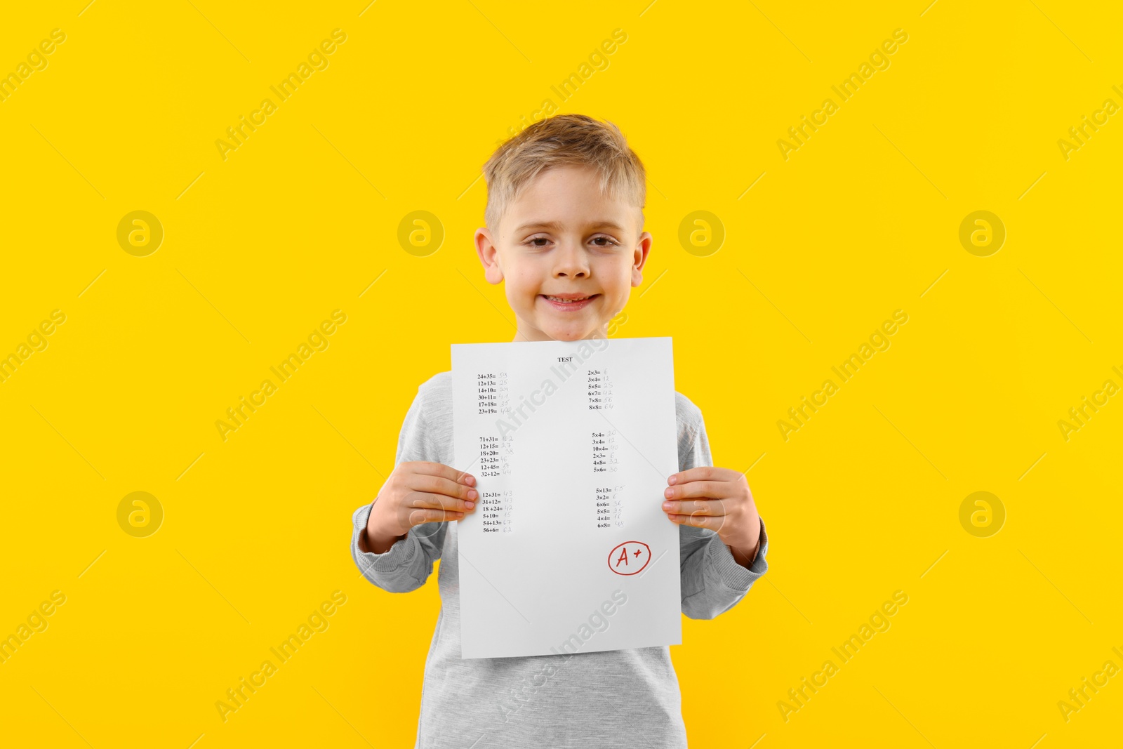 School grade. Little boy holding answer sheet with letter A and plus symbol on yellow background Photo of School grade. Little boy holding answer sheet with letter A and plus symbol on yellow background