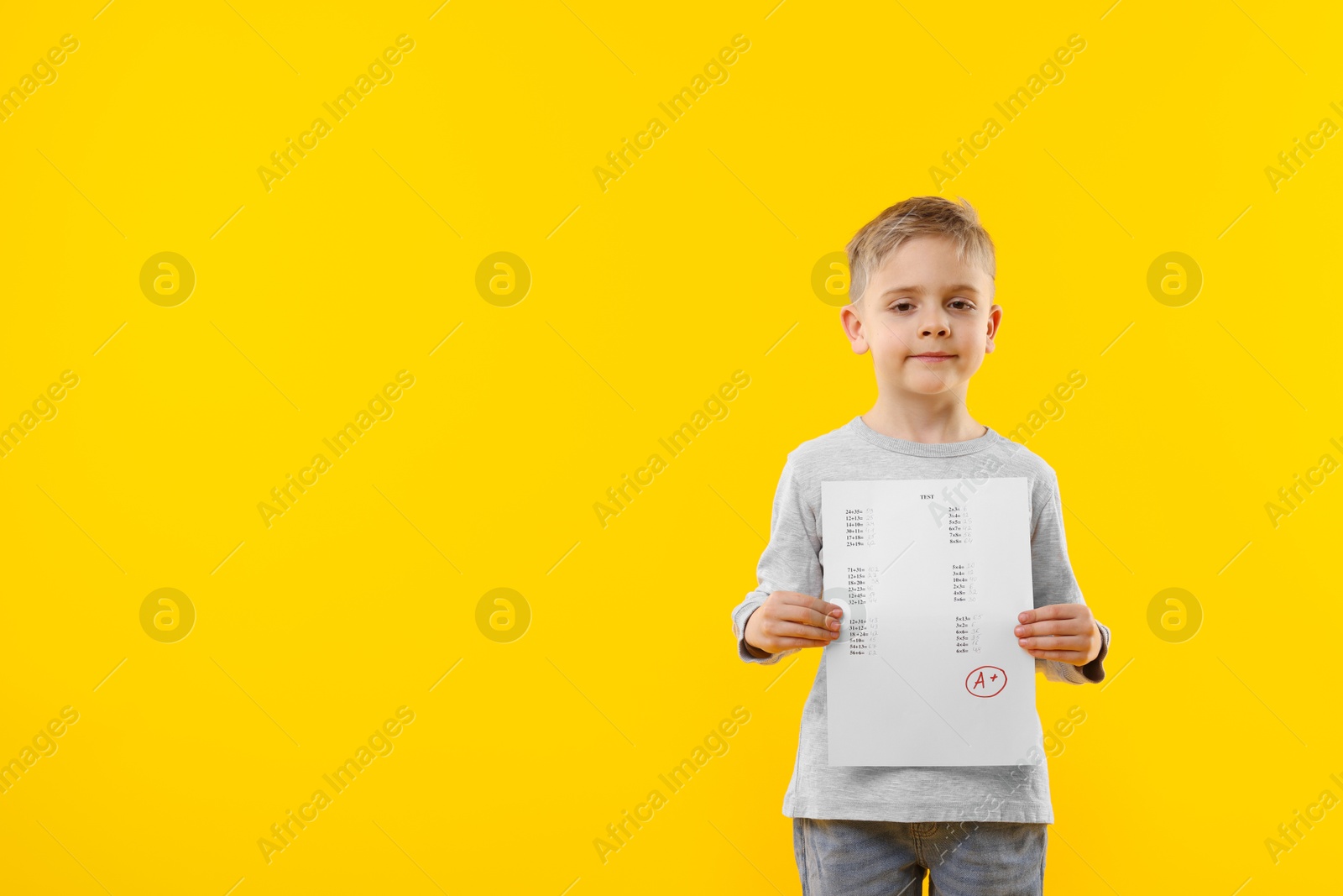 School grade. Little boy holding answer sheet with letter A and plus symbol on yellow background, space for text Photo of School grade. Little boy holding answer sheet with letter A and plus symbol on yellow background, space for text